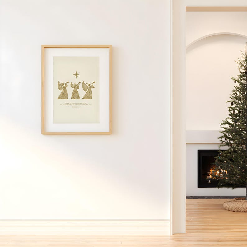 May include: A framed print featuring three golden angel figures playing trumpets beneath a star. The artwork has a light beige background and is set in a light wood frame. The print is hanging on a white wall.
