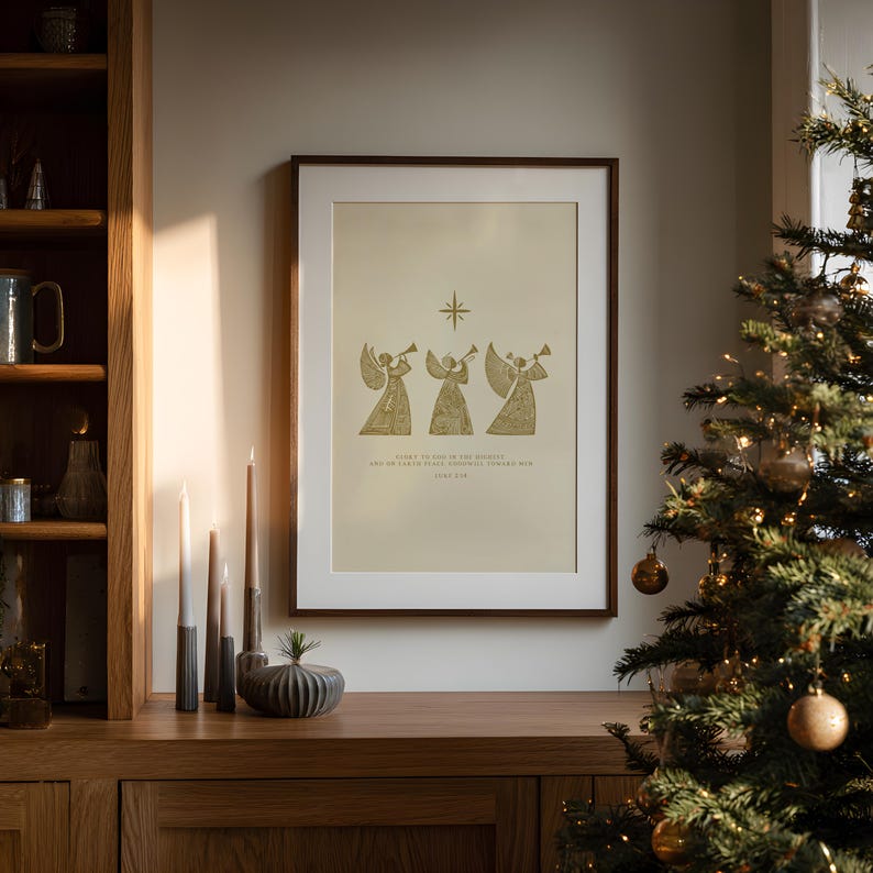 May include: Framed print featuring three golden angels playing trumpets, with a star above them. The print has text below the angels. The frame is brown, and the print is displayed on a wooden surface.