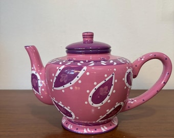 Tetera de cerámica con estampado floral en tonos rosa y morado, pintada a mano.