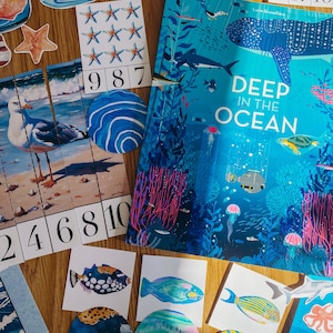 May include: An assortment of ocean-themed educational materials and illustrations. Features a book titled "Deep in the Ocean", fish and starfish cutouts, and number puzzles. The colour scheme includes blues, greens, and oranges, creating a vibrant and engaging visual.