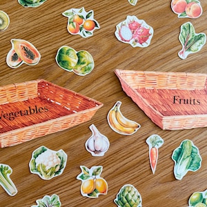 May include: A wooden table with two wicker baskets labeled "Vegetables" and "Fruits".  The baskets are filled with colorful cut-out images of various fruits and vegetables.