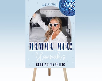 May include: A blue and white welcome sign with a disco ball and a photo of a woman wearing heart-shaped sunglasses. The sign says "Welcome, Mamma Mia! Hannah's Getting Married!"
