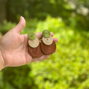 Pode incluir: Um par de brincos pendentes com tr&ecirc;s discos circulares sobrepostos feitos de fio enrolado. O disco superior &eacute; verde-lim&atilde;o, o disco do meio &eacute; bege e o disco inferior &eacute; castanho-escuro. Cada brinco &eacute; composto por estes tr&ecirc;s c&iacute;rculos coloridos.
