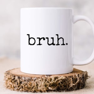 May include: White ceramic coffee mug with a black inscription that reads "bruh."