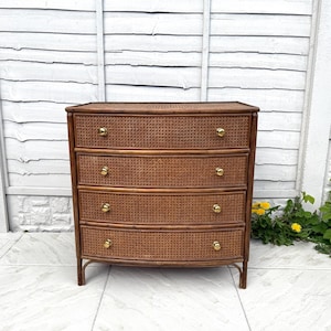 Puede incluir: Cómoda vintage de cuatro cajones hecha de ratán tejido y madera. La cómoda tiene un frente curvo y pomos de latón. El marco es de color marrón oscuro y los cajones son de un marrón más claro. La cómoda mide aproximadamente 76 cm de ancho, 41 cm de profundidad y 81 cm de alto.