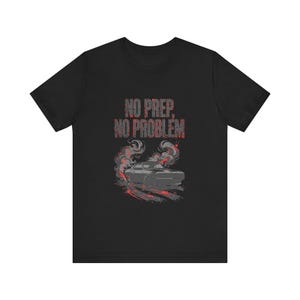 Peut inclure: Un t-shirt noir à manches courtes avec un motif représentant une voiture grise entourée de fumée rouge et grise. Le texte NO PREP, NO PROBLEM est imprimé en lettres rouges et grises usées au-dessus, avec des traces de pneus rouges au sol.