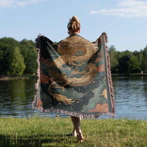 A person standing on grass near a body of water, holding a colorful, patterned blanket or shawl.