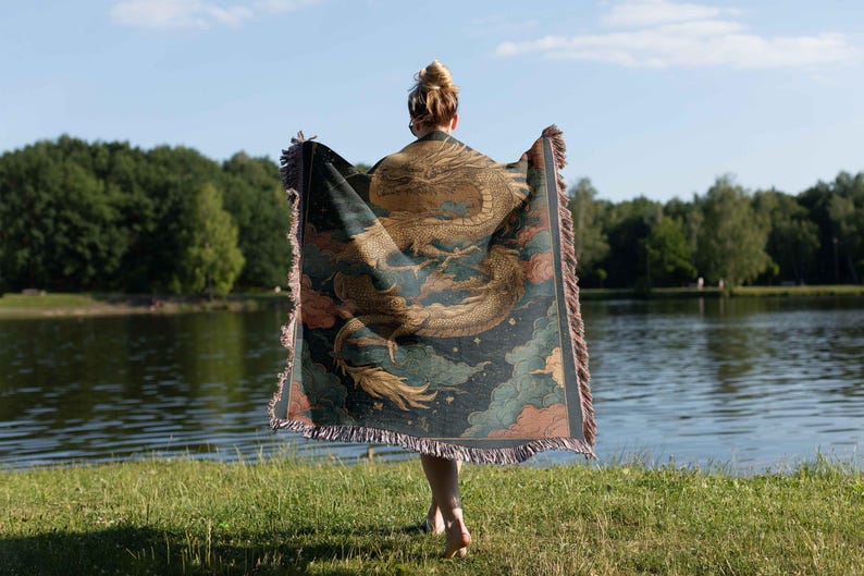 A person standing on grass near a body of water, holding a colorful, patterned blanket or shawl.