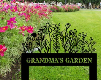 May include: Black metal garden sign with a floral silhouette design. The sign reads "GRANDMA'S GARDEN" in a bold font. The sign is placed in a garden with vibrant pink and purple flowers and green grass.