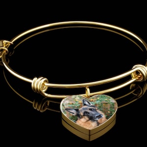 May include: Gold charm bracelet with a heart-shaped charm featuring a German Shepherd dog. The charm is attached to a gold chain and the bracelet is adjustable.