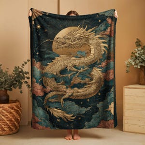 A person is holding up a large, intricately designed dragon blanket with a detailed illustration of a dragon and a moon-like figure against a night sky background.