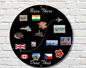 May include: A circular black metal magnetic board with the text Been There Done That in silver lettering. The board features a dashed flight path, a silver aeroplane icon, and various travel-themed magnets including flags, landmarks, and city scenes.