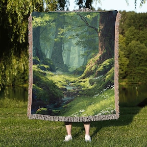 May include: A woven throw blanket featuring a detailed forest scene with a stream, lush greenery, and tall trees. The blanket has a fringed edge and is predominantly green, brown, and white. The image evokes a sense of nature and tranquility.