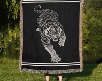 May include: Black woven throw blanket featuring a detailed white tiger design. The blanket has a fringed edge and white stripes near the top and bottom. The tiger is depicted in a dynamic, leaping pose.
