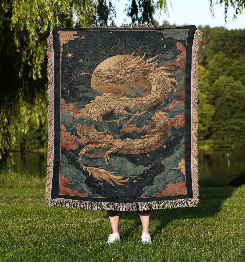 A person is standing in a grassy area, holding a large tapestry or blanket featuring a dragon and a starry night sky.
