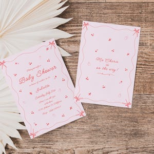 May include: Two pink baby shower invitations with red and white text. The larger invitation says "Baby Shower" and includes details about the event. The smaller invitation says "Ma Cherie is on the way!"