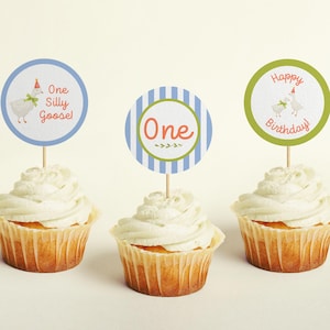 May include: Three cupcakes with white frosting and blue, green, and striped cupcake toppers. The toppers feature a goose with a party hat and the text "One Silly Goose!" "One" and "Happy Birthday".