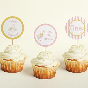 May include: Three cupcakes with pink and gold frosting and toppers. The toppers say "Happy Birthday", "One Silly Goose", and "One".