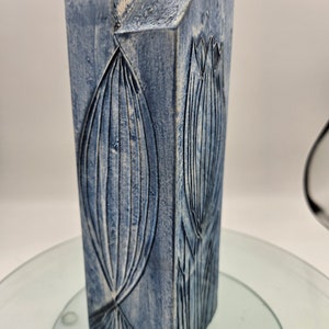 Peut inclure: Un vase en céramique bleu avec un motif géométrique et un glaçage blanc. Le vase a une forme rectangulaire avec un sommet légèrement arrondi et une surface texturée.