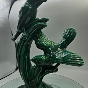 Peut inclure: Une sculpture en céramique verte de trois oiseaux perchés sur une branche feuillue. Les oiseaux sont stylisés et ont une finition brillante.