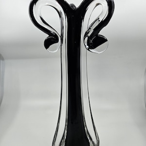 May include: A tall, elegant glass vase with a striking black and clear design. The vase features a slender, elongated body with a flared base. The top has two curved, loop-like handles. The vase is approximately 35.5 cm tall.