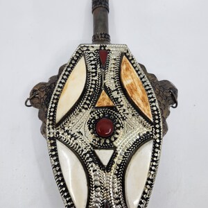 May include: An antique flask with a silver-coloured metal body. It features cream and brown inlaid accents, and red gemstones. The top is dark metal with a cylindrical shape. The flask has a decorative, textured design. The flask is likely made of metal.