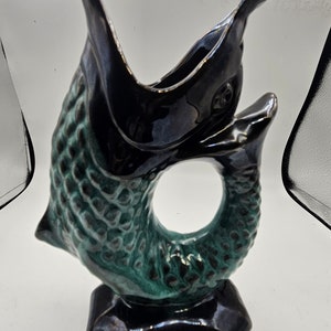 May include: A ceramic vase shaped like a fish with a green and black glaze. The fish is curled into a circle with its tail in its mouth. The vase has a black base.