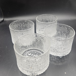 Puede incluir: Cuatro vasos de beber de vidrio transparente con una superficie texturizada. Los vasos están apilados uno encima del otro.