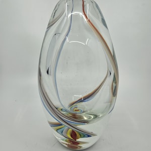 May include: Clear glass vase with an oval shape. The vase has colourful swirls of blue, red, and brown glass. The design is a mix of abstract and organic shapes, creating a decorative piece.