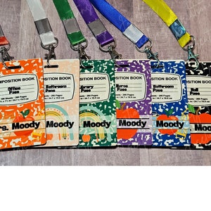 May include: Six teacher ID badges, each resembling a composition book, with lanyards. The badges display different locations such as "Office" and "Bathroom", and feature the name "Moody". The designs include an apple motif. Measurements are 9 x 7 inches / 24.7 x 19.0 cm.