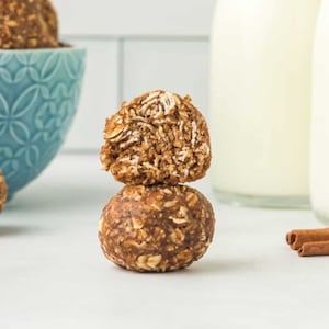 May include: Two brown and beige oatmeal energy balls, one with a bite taken out, on a white surface.