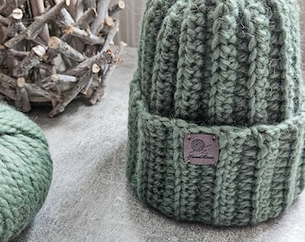 May include: A sage green knitted beanie with a brown leather label that says "Hand Made".