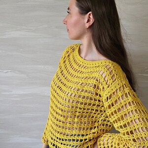 May include: A yellow crochet top with a loose fit and long sleeves. The top has a  crochet pattern with large open squares.