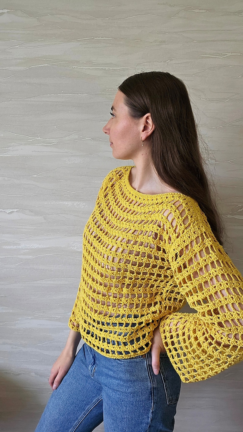May include: A yellow crochet top with a loose fit and long sleeves. The top has a  crochet pattern with large open squares.