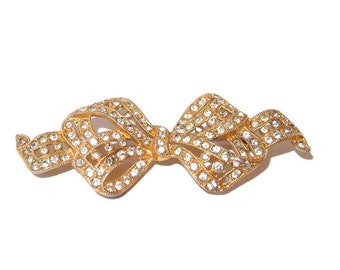 May include: A gold-toned bow brooch, encrusted with clear crystals. The bow design features intricate detailing and a secure pin backing. This elegant accessory is suitable for adding a touch of sparkle to any outfit.