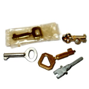 May include: A collection of vintage keys in various shapes and sizes. The keys are made of metal and include a gold-colored key with a pearl accent, a silver key, and a key still in its original packaging.
