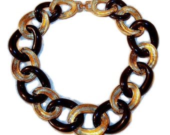 May include: A chunky necklace with large, oval links in black and gold. The gold links have a textured, glittery finish. The necklace is secured with a gold-toned clasp. A bold fashion accessory.