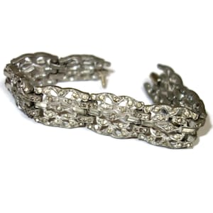 May include: Silver-toned bracelet with an openwork design. The bracelet features a series of interconnected links, each adorned with small, clear rhinestones. The links have an intricate, floral-inspired pattern, creating a delicate and elegant appearance.