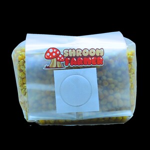 May include: A clear plastic bag with a white label that says "SHROOM FARMER" and a red mushroom graphic. The bag contains a yellow grain substrate.