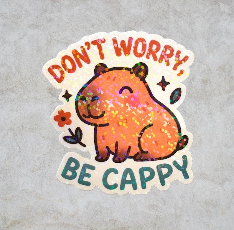 This sticker features an adorable, cartoon-style capybara sitting contentedly with a big, peaceful smile and closed eyes. The capybara has a light brown body with darker brown accents for the ears, outline, and tiny fur markings.  Above the capybara, the text reads “DON’T WORRY,” in playful, rounded orange letters. Below the capybara, the phrase “BE CAPPY” is written in bold, teal-blue bubble letters — a clever pun combining “happy” and “capybara.”