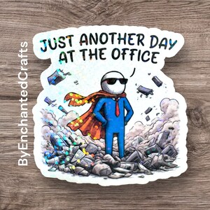 A rectangular vinyl sticker featuring a minimalist, retro-inspired design. The text reads "Just Another Day At The Office" in a bold, vintage-style serif font. Below the text is a simple line-art illustration of a traditional office building with a small flag on top. The sticker has a clean, white background with a thin black border, perfect for laptop or water bottle decoration.