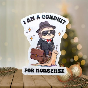 May include: A whimsical sticker featuring a sloth in a suit and sunglasses riding a snail, holding a briefcase. The text reads "I AM A CONDUIT FOR NONSENSE". The sticker has a white background with gold star accents and is set against a blurred holiday background.