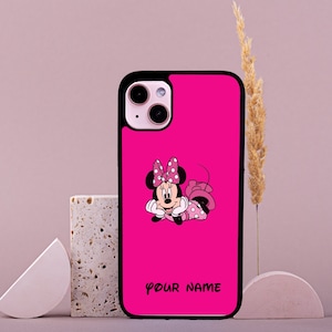 Puede incluir: Una funda de teléfono rosa con borde negro. La funda presenta una imagen de dibujos animados de Minnie Mouse con un vestido rosa con lunares blancos. El texto "YOUR NAME" está impreso en negro en la parte inferior de la funda.