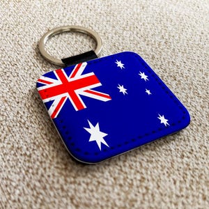 May include: Square keychain featuring the Australian flag. The design includes a blue background with the Union Jack in the upper left corner and white stars. The keychain has a silver ring and a black strap.