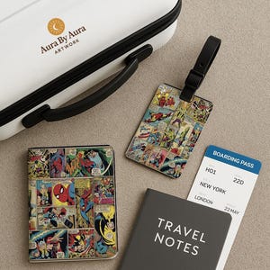 Puede incluir: Una maleta de viaje blanca con asa negra y el texto "Aura By Aura ARTWORK". Un tarjetero, una etiqueta de equipaje y un cuaderno presentan arte de cómic. También se ve una tarjeta de embarque.