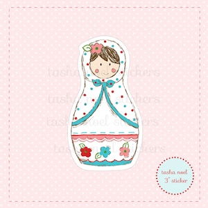 May include: A sticker depicting a cartoon Russian nesting doll. The doll is white with blue and red polka dots, a blue bow, and floral details. The sticker is 7.6 cm in size and has the text "tasha noel 3" sticker".