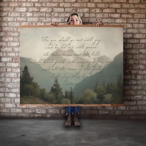 Peut inclure: Une grande affiche murale avec une peinture de paysage de montagnes et d'arbres dans des tons verts et gris sourds. L'impression comprend une écriture avec le texte "For you shall go out with joy..." et le verset biblique Isaïe 55:12.