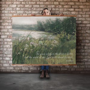 May include: A large rectangular canvas print with a landscape painting featuring a river, tall grass, and flowers. The print has a wooden frame and includes the text "The grass withers, the flower fades, but the word of our God will stand forever."