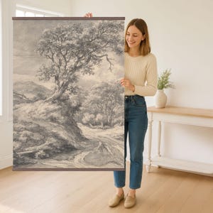 May include: A black and white landscape drawing of a winding path through a forest with a large tree in the foreground. The drawing is on a canvas and is being held by a person.