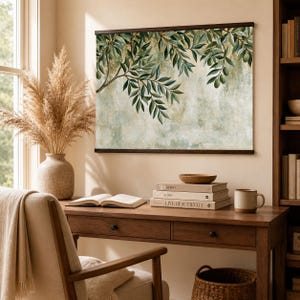 May include: A framed wall art print featuring a watercolor olive branch design with green leaves and olives. The artwork is displayed above a wooden desk with books, a mug, and a vase with dried plants. The overall aesthetic is natural and serene.